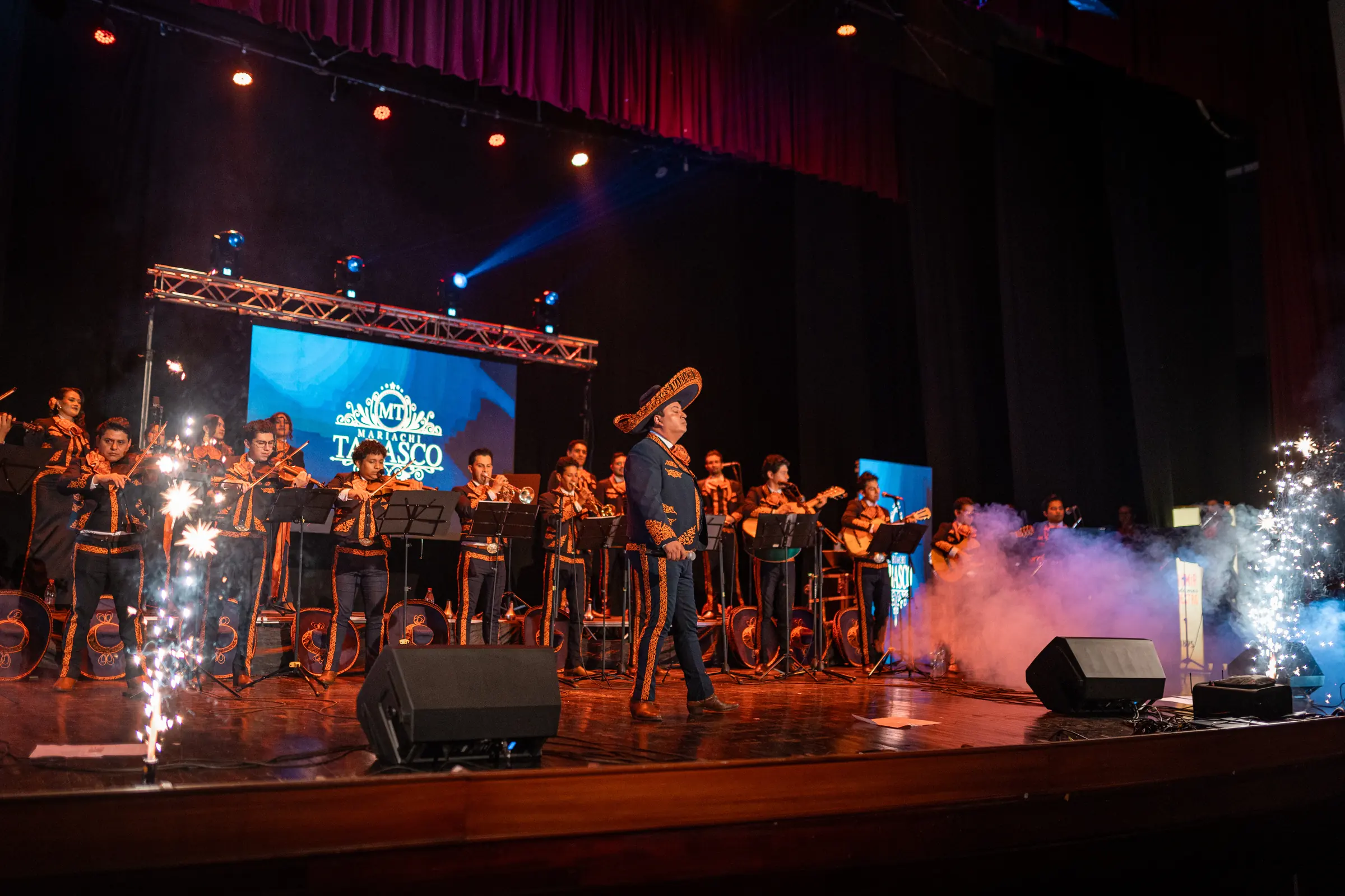 Mariachi Tabasco en concierto en un teatro, con el cantante al centro y chispas de luz