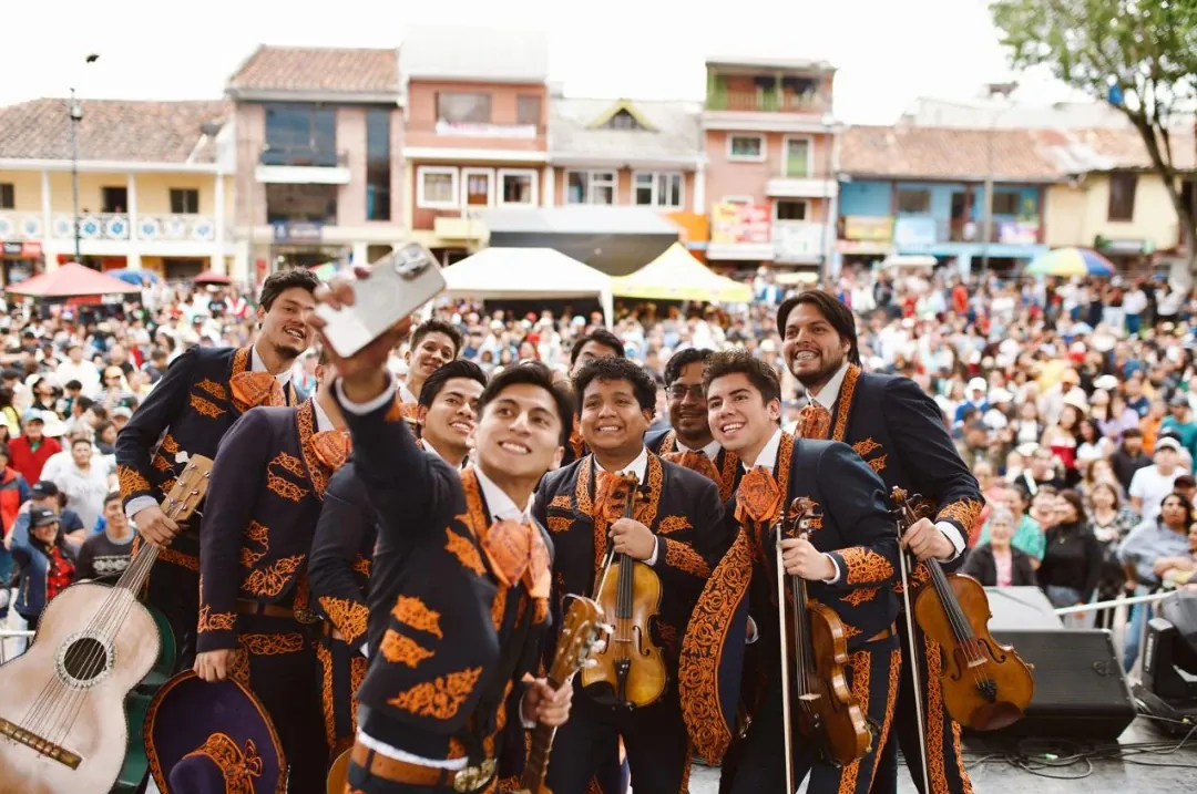 Músicos de Mariachi Tabasco tomándose una selfie con sus instrumentos frente al público en una plaza