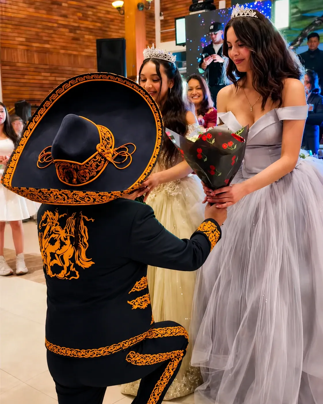 El Patrón Cuenca de rodillas entregando un ramo de flores a dos quinceañeras
