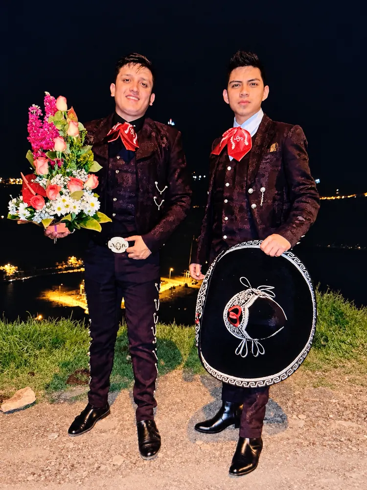 Dos integrantes de Mariachi Tabasco con flores y sombrero, de noche